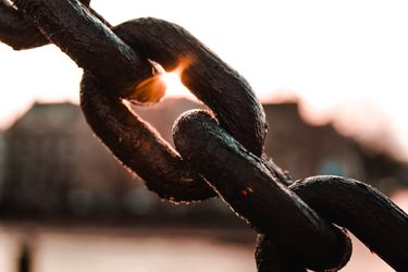 Close-up of a metal chain with sunlight shining through the links against a blurred background.