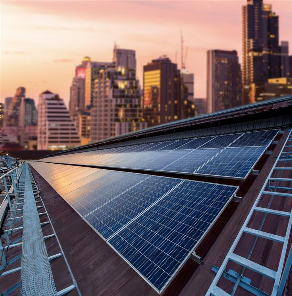 Rooftop solar panels with a city skyline in the background during sunset.